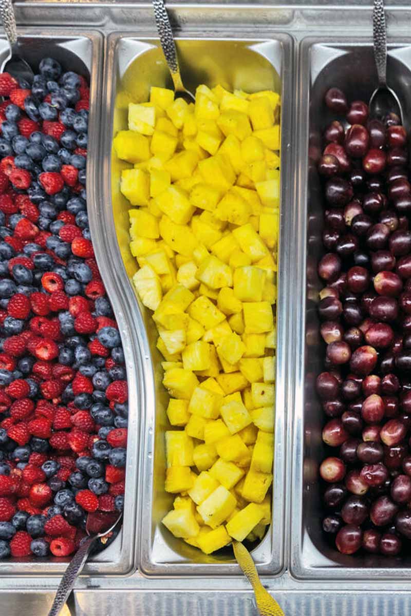 A colorful fruit buffet with neatly arranged trays of mixed berries, pineapple chunks, and grapes.