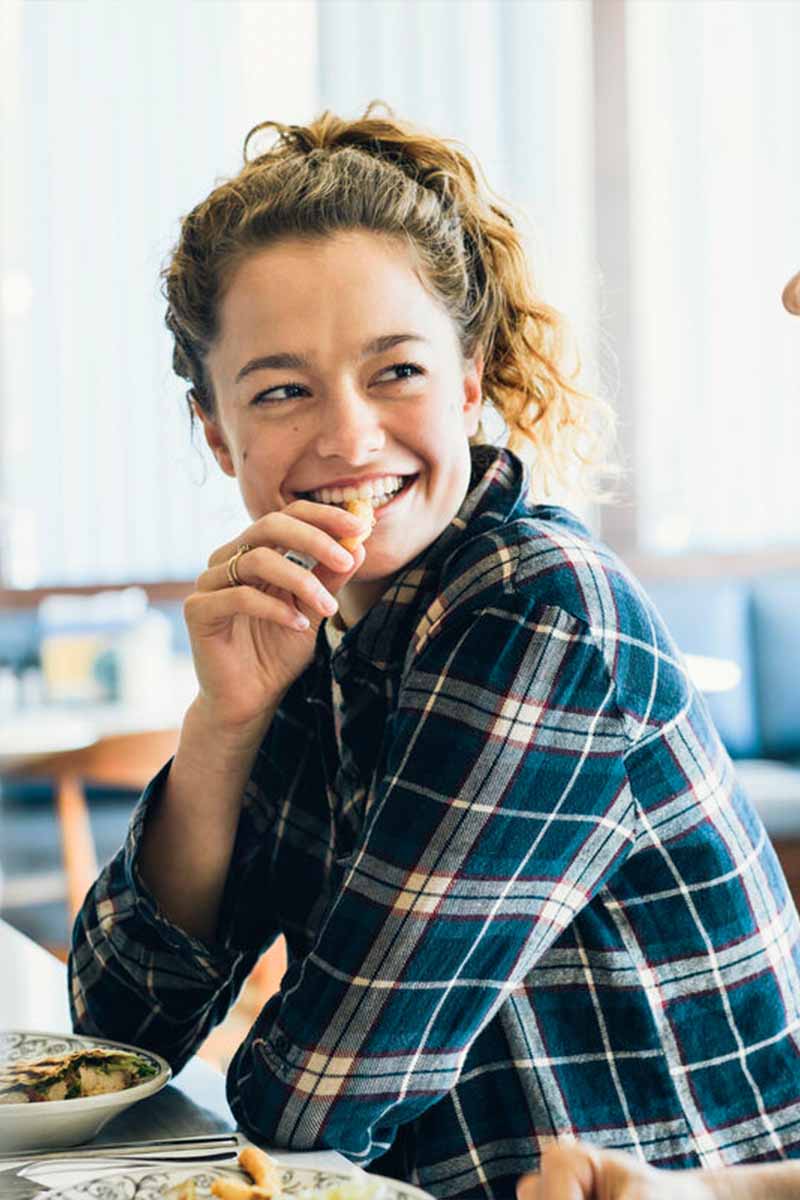 Two people sitting at a table in a casual dining setting, with one person smiling warmly while looking at the other during their conversation.