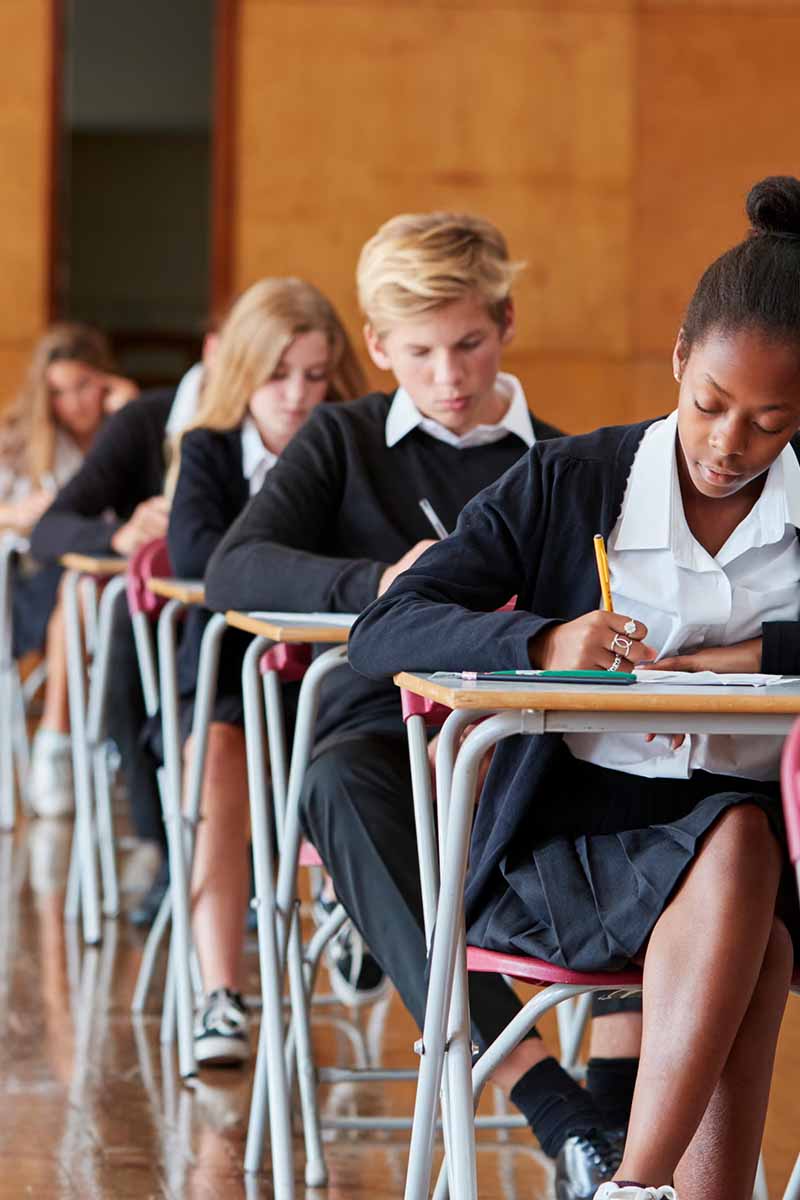 Students in private school uniform sitting at desk, taking a test while looking at their work. loading=